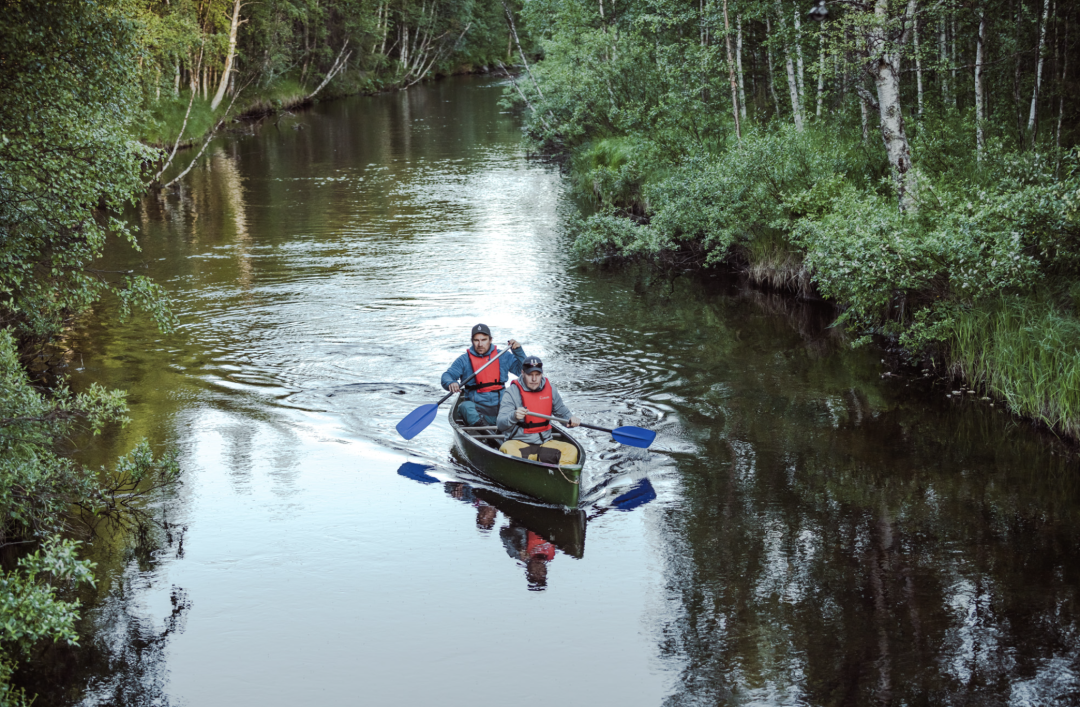 A canoe with two people rowing it in beautiful Pyhäjoki surrounded by summer greenery of the forest