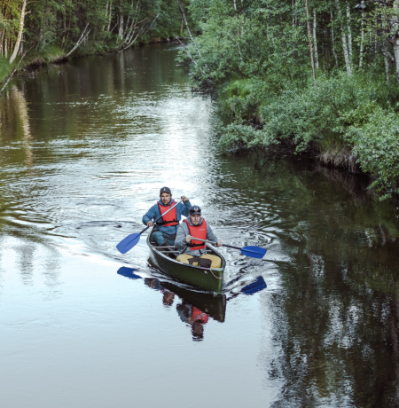 A canoe with two people rowing it in beautiful Pyhäjoki surrounded by summer greenery of the forest