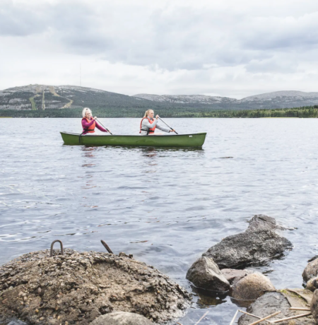 Kaksi henkilöä kanootilla melomassa Pyhäjärvellä pilvisenä kesäpäivänä lähes tyynellä säällä Pyhätunturi uljaasti taustalla