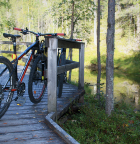Maastopyörä nojailemassa puisen rakenteen aitaan joen/puron varrella loppu kesän vihreässä maisemassa