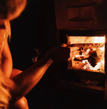 Henkilö laittamassa saunan loimuavaan kiukaan tulipesään lisää puita. 