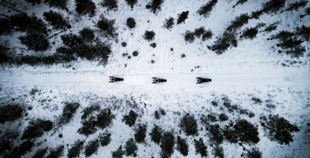 Snowmobiles from above with a drone, driving through a forest in Finland