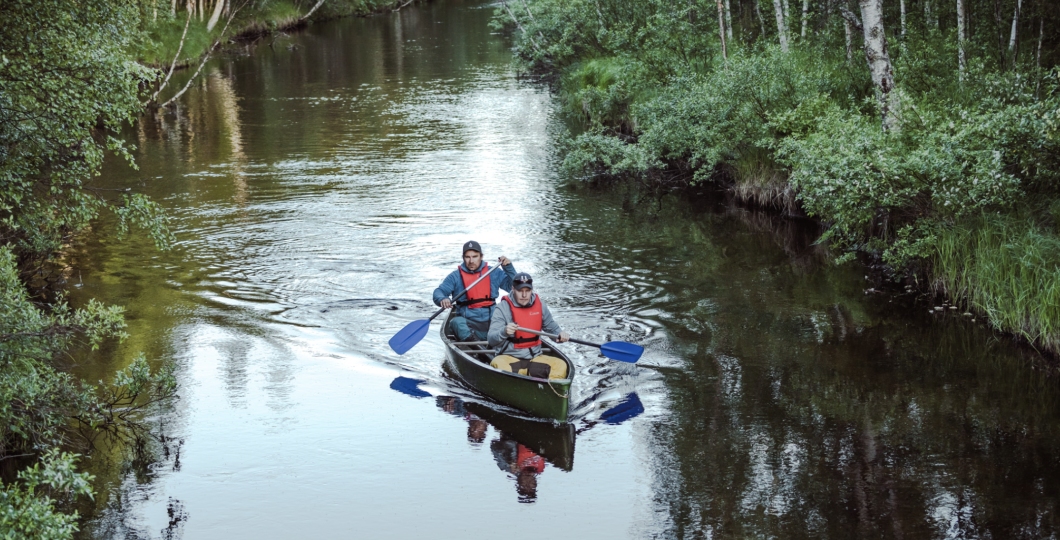 A canoe with two people rowing it in beautiful Pyhäjoki surrounded by summer greenery of the forest