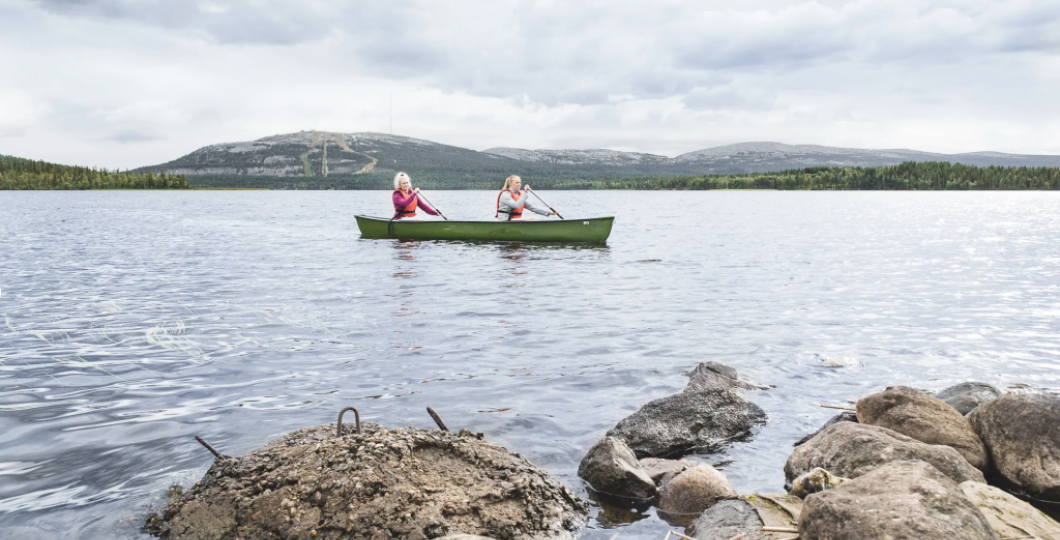 Kaksi henkilöä kanootilla melomassa Pyhäjärvellä pilvisenä kesäpäivänä lähes tyynellä säällä Pyhätunturi uljaasti taustalla